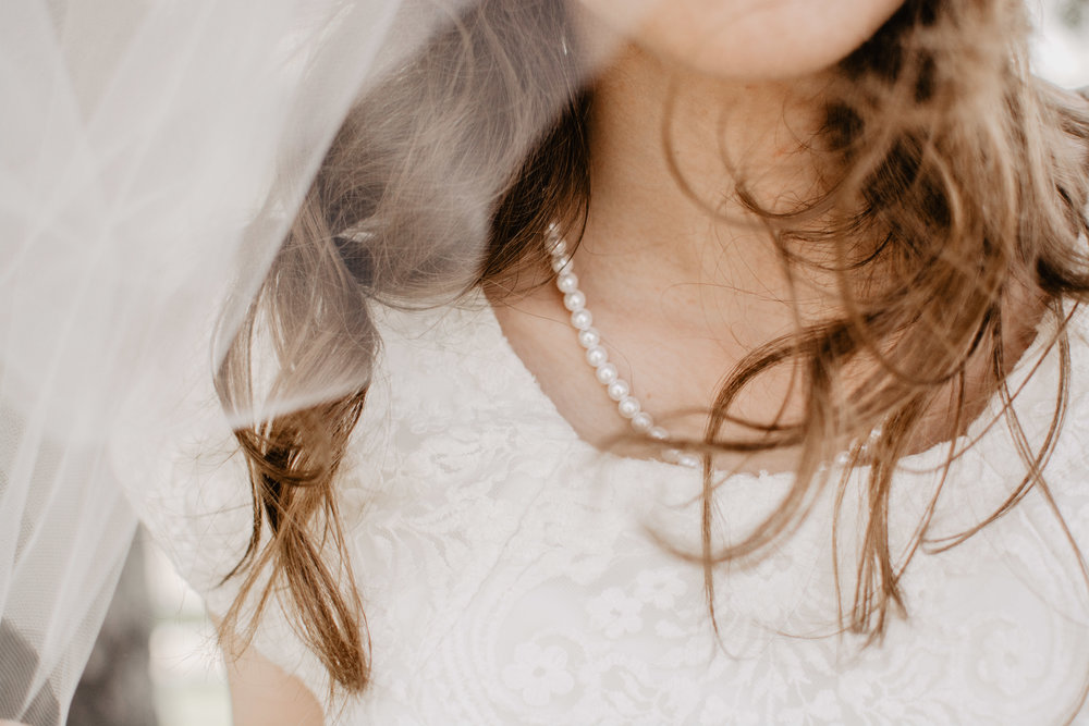 bride with wind blown hair and a beautiful strand of pearls at Logan Utah wedding