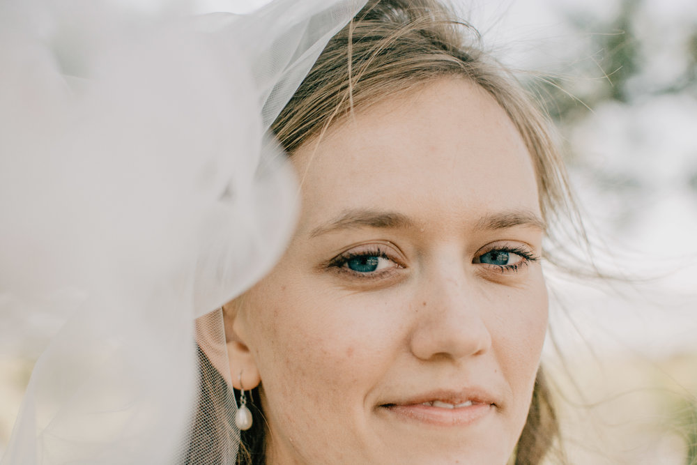 Bride with wind blown hair and pearl earrings at Logan Utah temple grounds