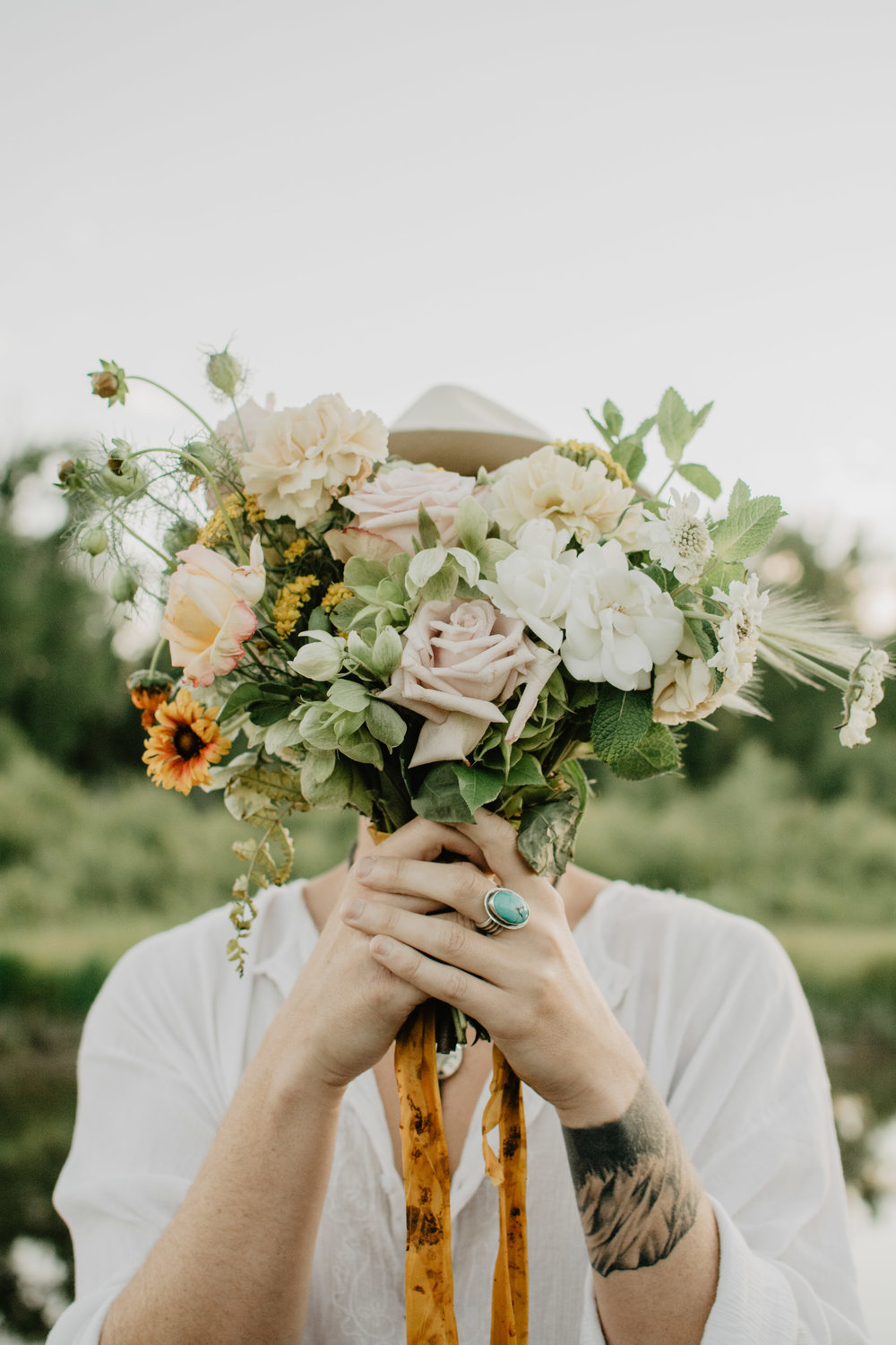 Boho groom with the brides flowers holding them in front of his face for their Jackson Hole wedding