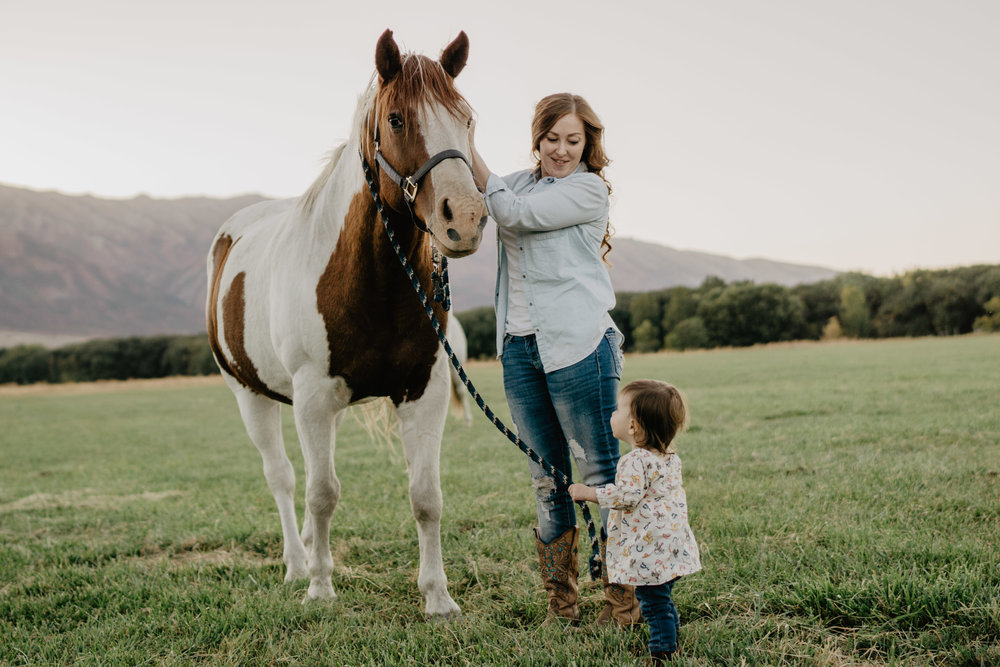 mother with her toddler in a field together enjoying a horse
