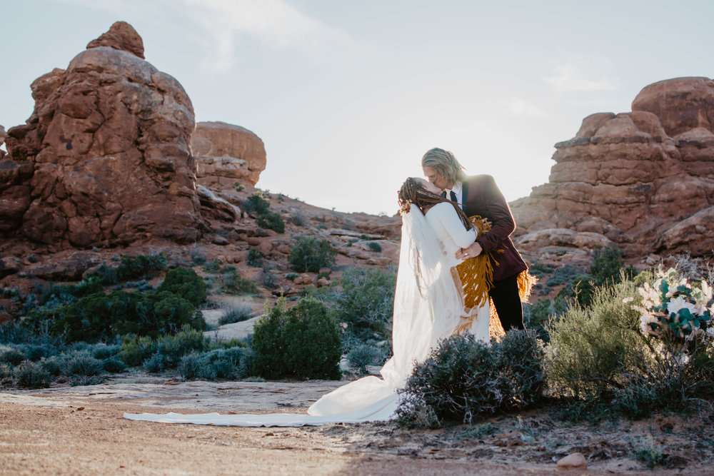 Jocilyn Bennett Photography | Destination Wedding Photographer | Elopement Wedding Photographer | National Park Elopement Photography | Capturing raw and genuine emotion | Utah Photographer | Utah wedding Photographer| National Park Weddings | Adventure Photographer | Bohemian photography | Bohemian wedding | Arches wedding | Arches National Park | Bride with dreads | Candid Bridal Photos | ASOS red suit coat | Handmade bridal gown | Bride and Groom kissing in the red rock |