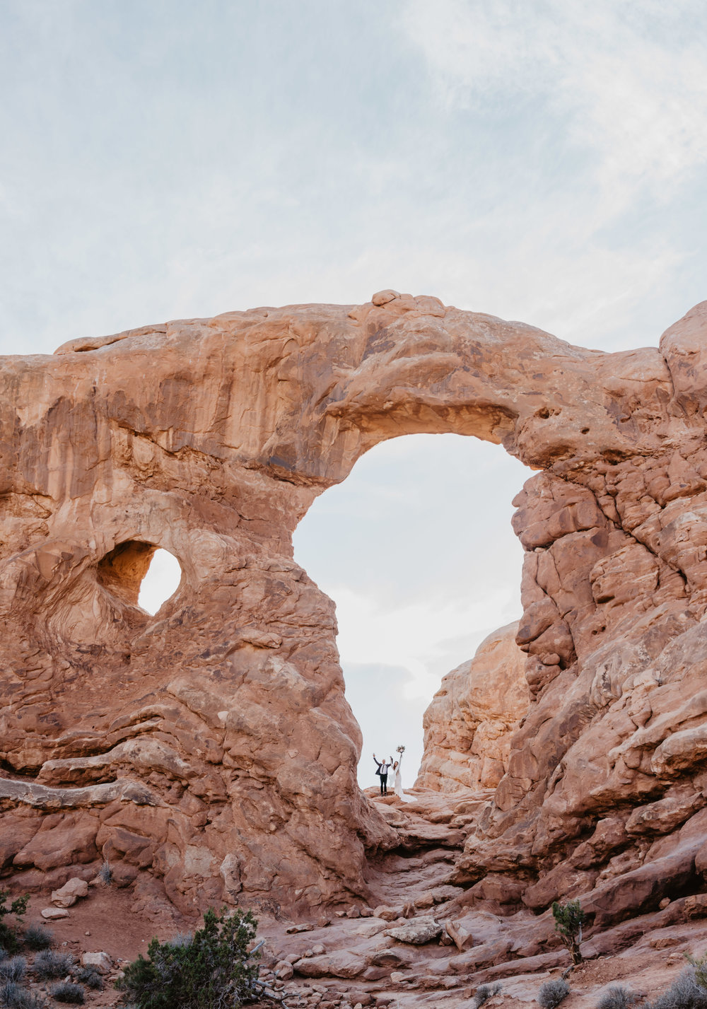 the arches in southern Utah with a boho bride and groom holding hands and shouting as they elope Jocilyn Bennett Photography | How to Plan an Elopement | Why Elope | Reasons to Elope | Destination Wedding Photographer | Utah Wedding Photographer | Adventure Photographer | Destination Elopement Photographer | Traveling Photographer | Arches National Park | Arches National Park Elopement | Southern Utah Elopement | Boho Bride | Bride with dreads |