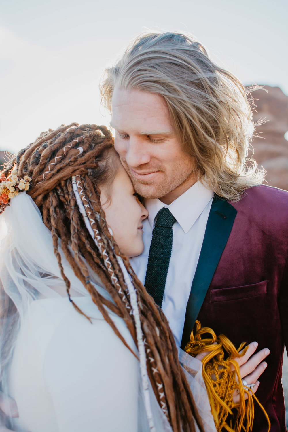 red headed bride who has dreads snuggles into her blonde grooms chest as he smiles down at her on their wedding day for their bridals Jocilyn Bennett Photography | How to Plan an Elopement | Why Elope | Reasons to Elope | Destination Wedding Photographer | Utah Wedding Photographer | Adventure Photographer | Destination Elopement Photographer | Traveling Photographer | Arches National Park | Arches National Park Elopement | Southern Utah Elopement | Boho Bride | Bride with dreads |