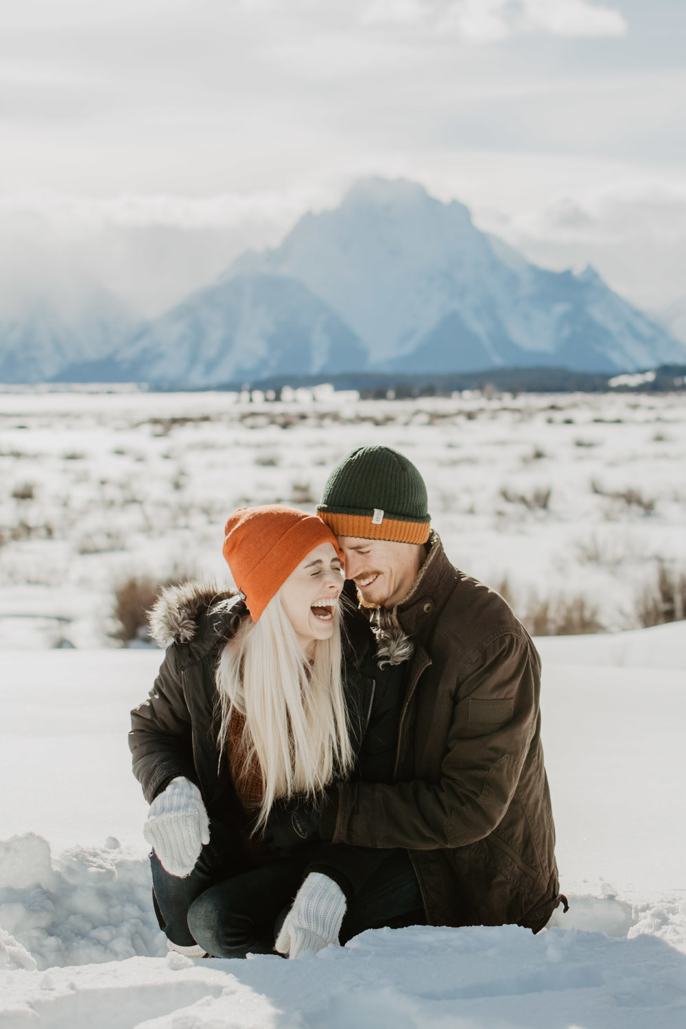 man and woman at their Grand Tetons winter engagement session laughing as they walk through the deep snow together | Jocilyn Bennett Photography | Winter Engagements | Snowy Engagements | Wyoming Engagement Photography | Utah Wedding Photographer | Winter Engagement Poses | What to Wear for Winter Engagements | Destination Wedding Photographer | Outfit ideas for Winter Engagements | Adventure Photographer | Wyoming Photographer | Winter Engagements in Jackson Hole | Jackson Hole Engagements | Wyoming Bride | Wyoming Wedding Photographer | Jackson Hole Wedding Photographer | 