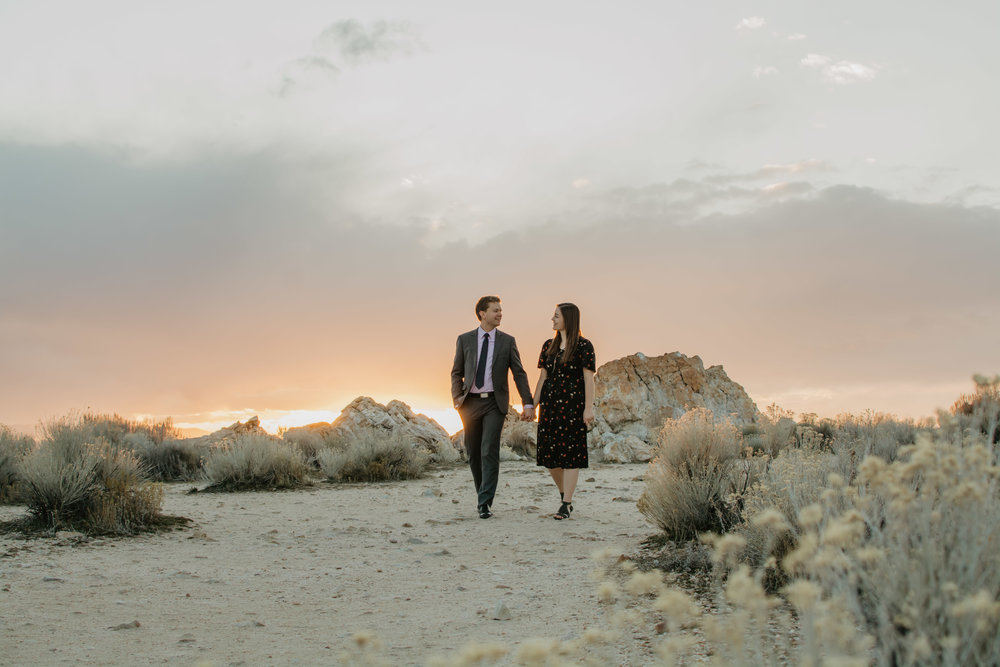 man and woman holding hands in the desert in Utah as the sun sets behind them with big storm clouds hovering over them as they look at each other and smile Jocilyn Bennett Photography | Destination Wedding Photographer | Elopement Wedding Photographer | National Park Elopement Photography | Capturing raw and genuine emotion | Utah Photographer | Utah wedding Photographer | National Park Weddings | Adventure Photographer | Antelope Island Engagements | Engagement pose ideas | Utah engagement photography | Engagement Pose Ideas | Candid Engagements |
