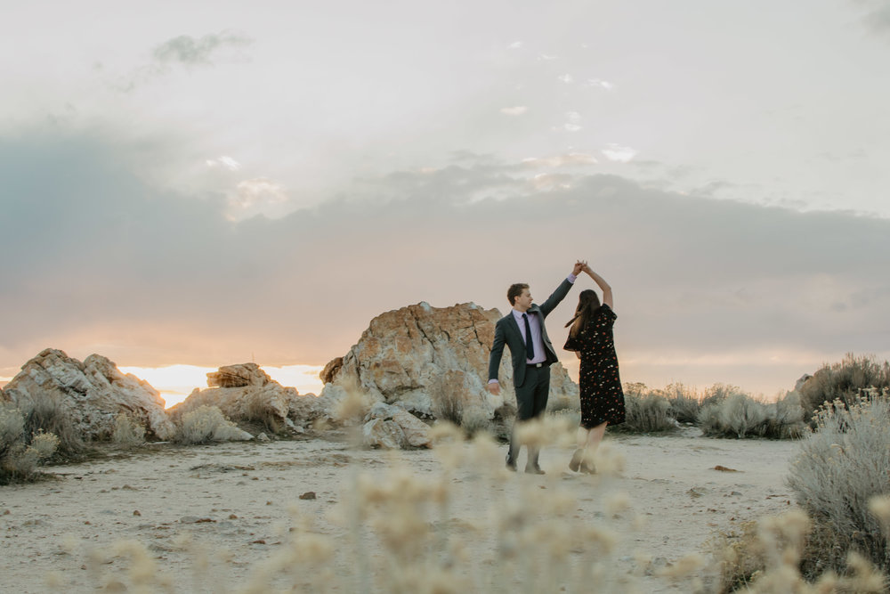 sunset engagement session with man dancing and twirling his fiance in the desert in Antelope Island with clouds and sun setting in the background Jocilyn Bennett Photography | Destination Wedding Photographer | Elopement Wedding Photographer | National Park Elopement Photography | Capturing raw and genuine emotion | Utah Photographer | Utah wedding Photographer | National Park Weddings | Adventure Photographer | Antelope Island Engagements | Engagement pose ideas | Utah engagement photography | Engagement Pose Ideas | Candid Engagements |
