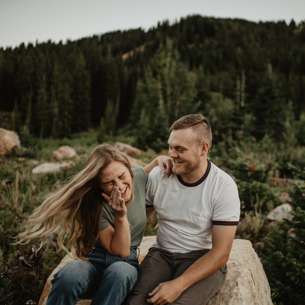 mountain summer session with man and woman sitting on a rock in the mountains and laughing with each other