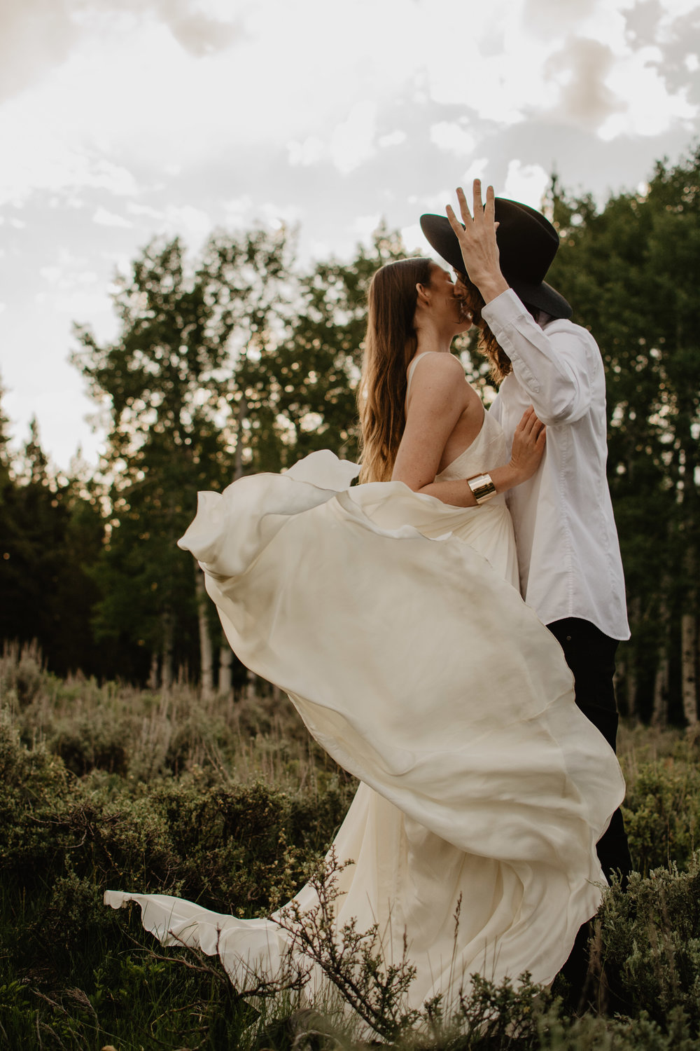 brides wedding dress flying in the wind as she kisses her groom for their Tetons bridals