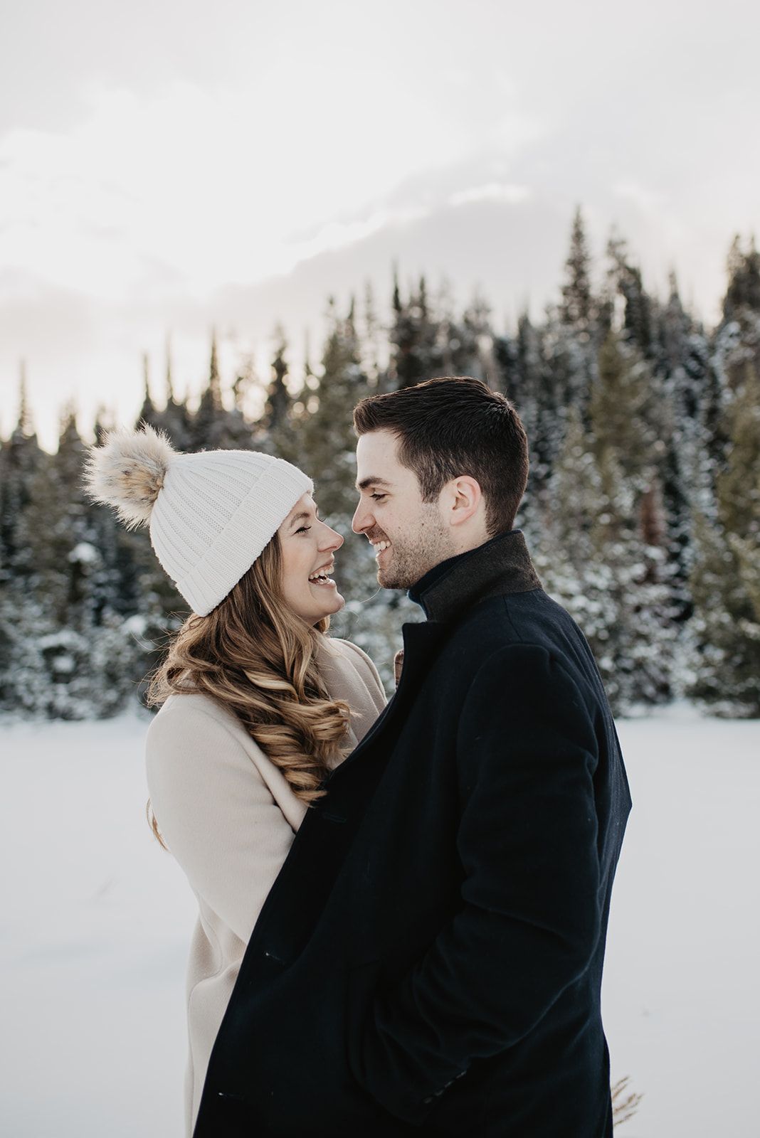 Jackson Hole winter engagement session with man and woman holding each other close while standing in the snow in front of tall green pine trees