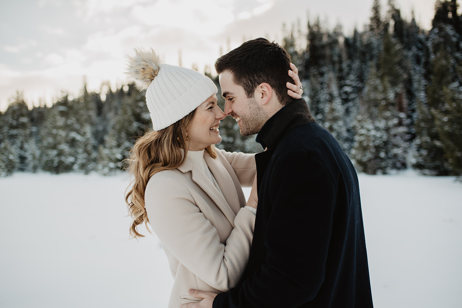 winter engagement session in Jackson Hole with snow surrounding the couple and beautiful pine trees covered in snow with the couple embracing each other