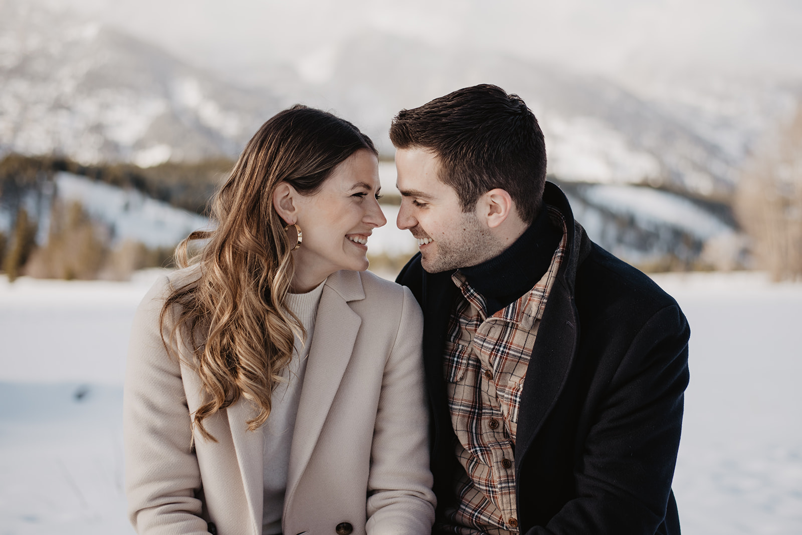 Jackson Hole winter engagement session with man and woman sitting with each other with their noses together smiling as they romantically look into each others eyes