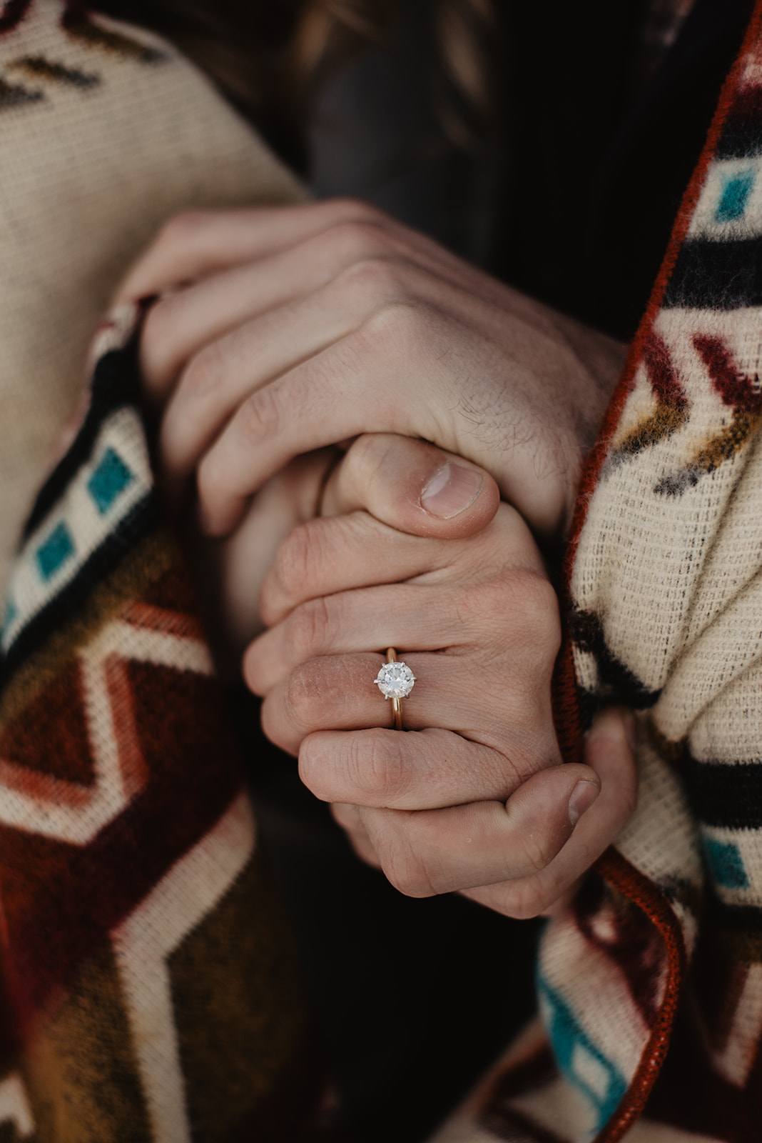 detail shot of engagement ring during a Jackson Hole winter engagement session with hand holding woman's hand and a tribal print wool blanket wrapped around them