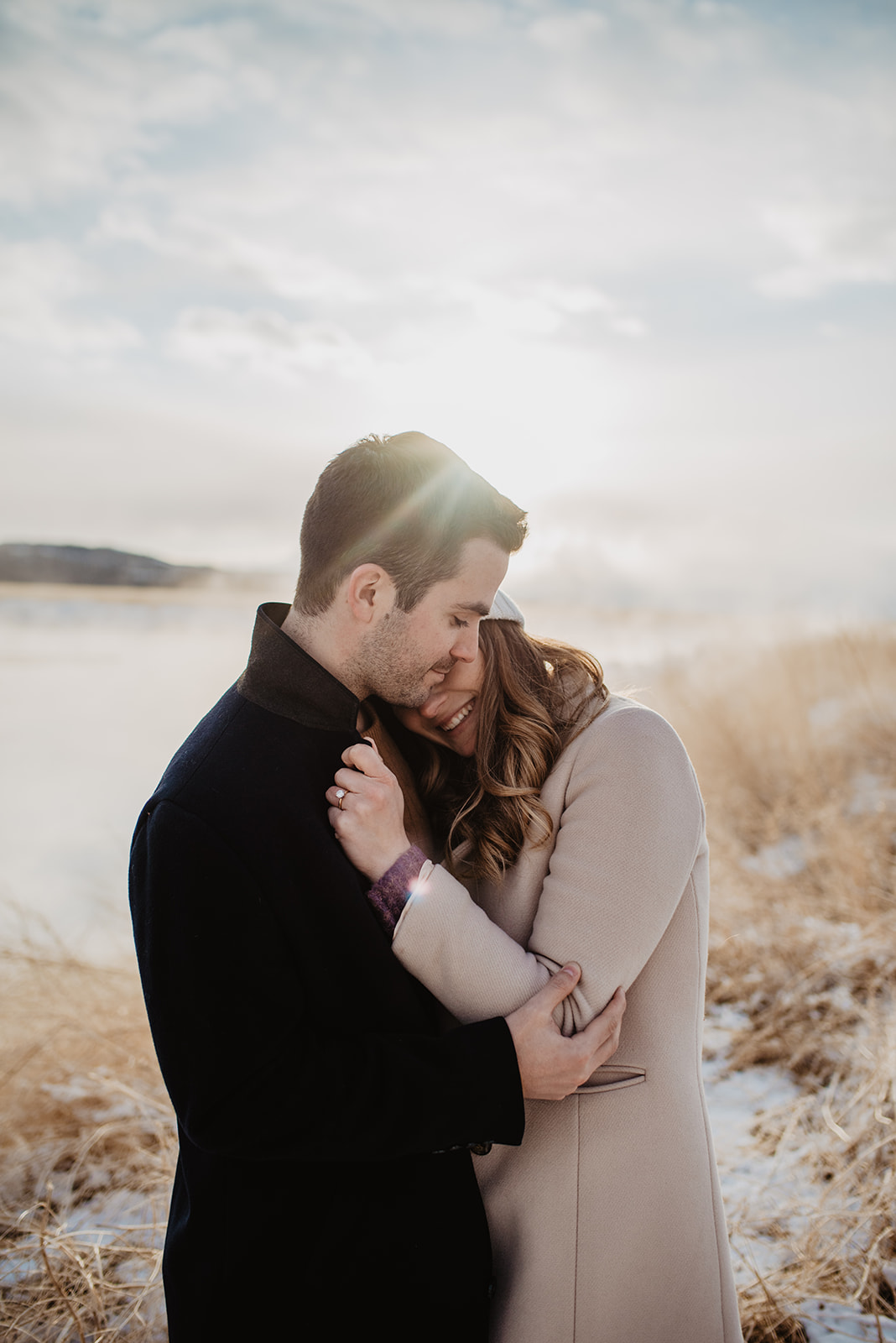 sunsetting behind a man and woman with the light gleaming behind them as the woman falls into the mans chest and he holds her by the arm in Jackson Hole for a winter engagement session