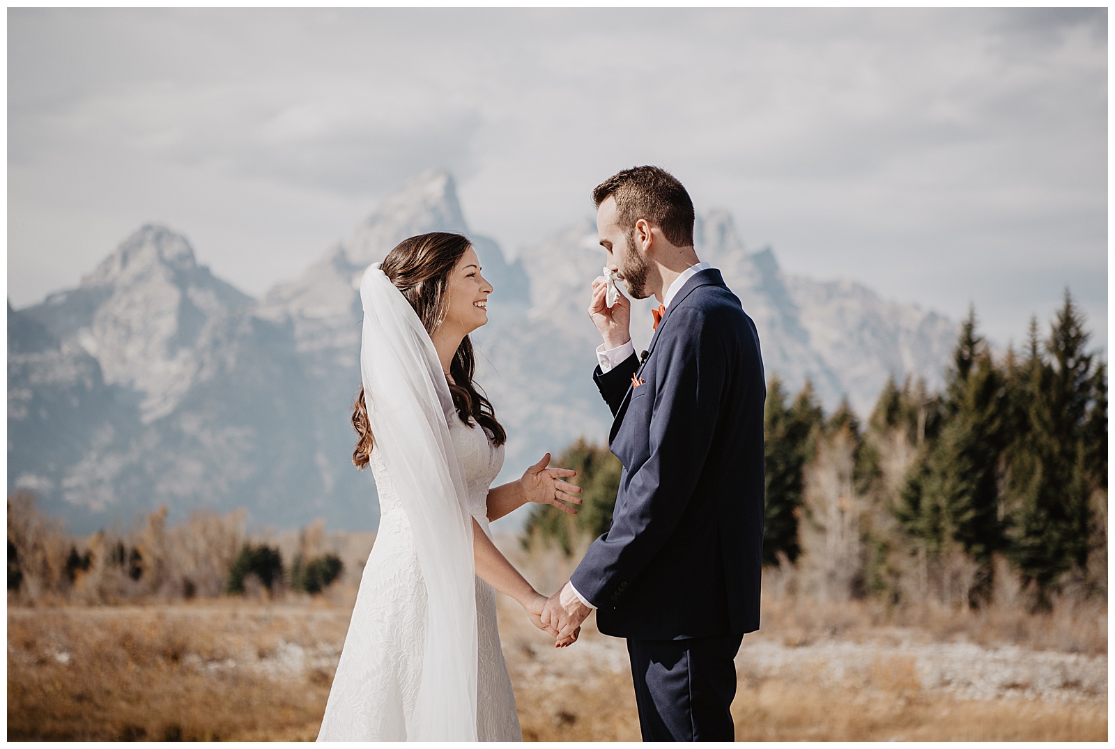 beautiful bride in a lace gown smiling at her groom as he wipes away tears during their fall wedding at Grand Teton National Park