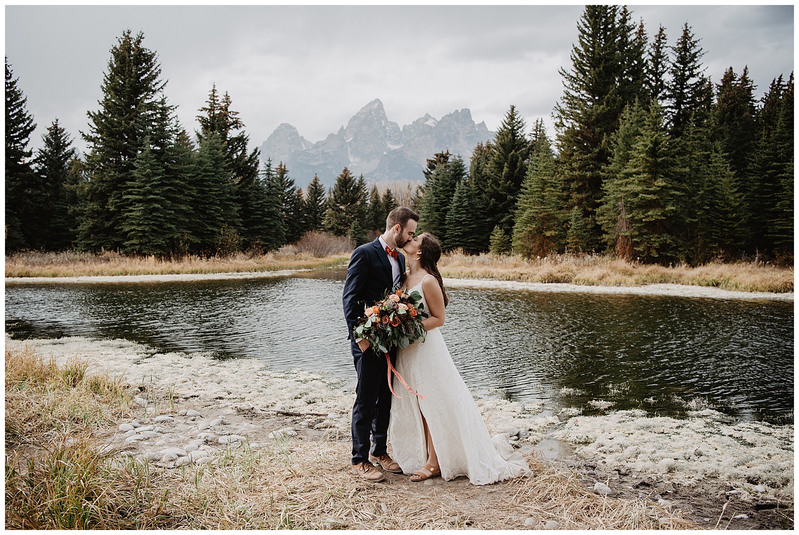 Grand Teton National Park fall wedding day with bride and groom standing in front of a river with tall trees and the Tetons behind them