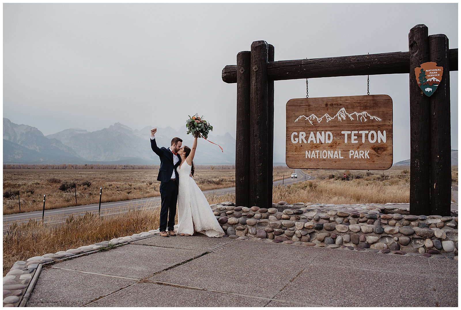 bride and groom on their Grand Teton wedding day standing next to a welcome sign to the national park kissing each other with their arms in the air
