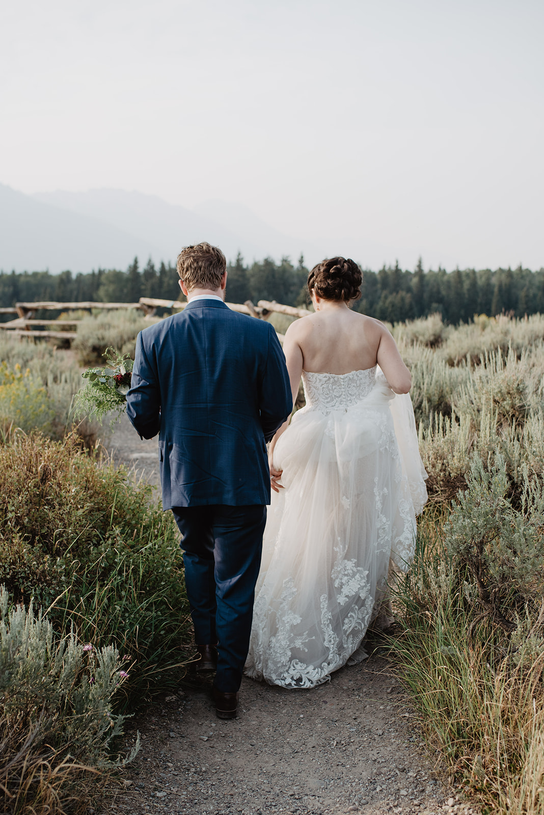 Bride and groom holding hands and walking away from the camera while they are on a dirt trail in Jackson Hole in their wedding attire