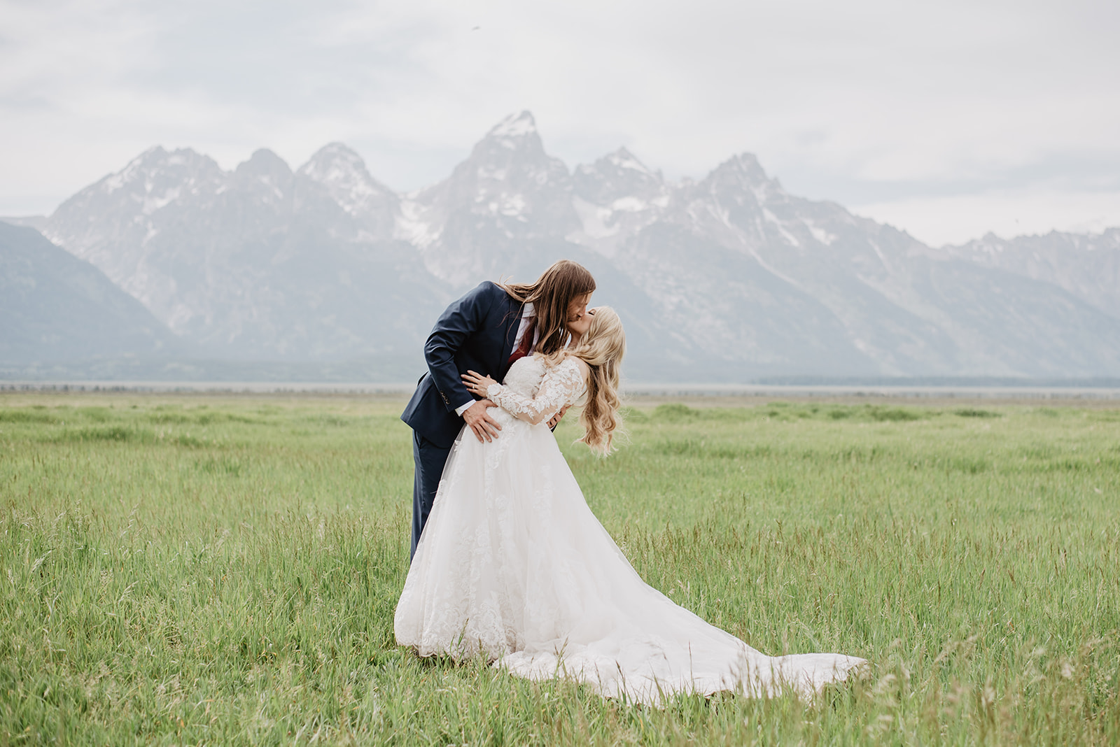 groom dipping his bride in a green spring field in Jackson Hole with the Tetons behind them
