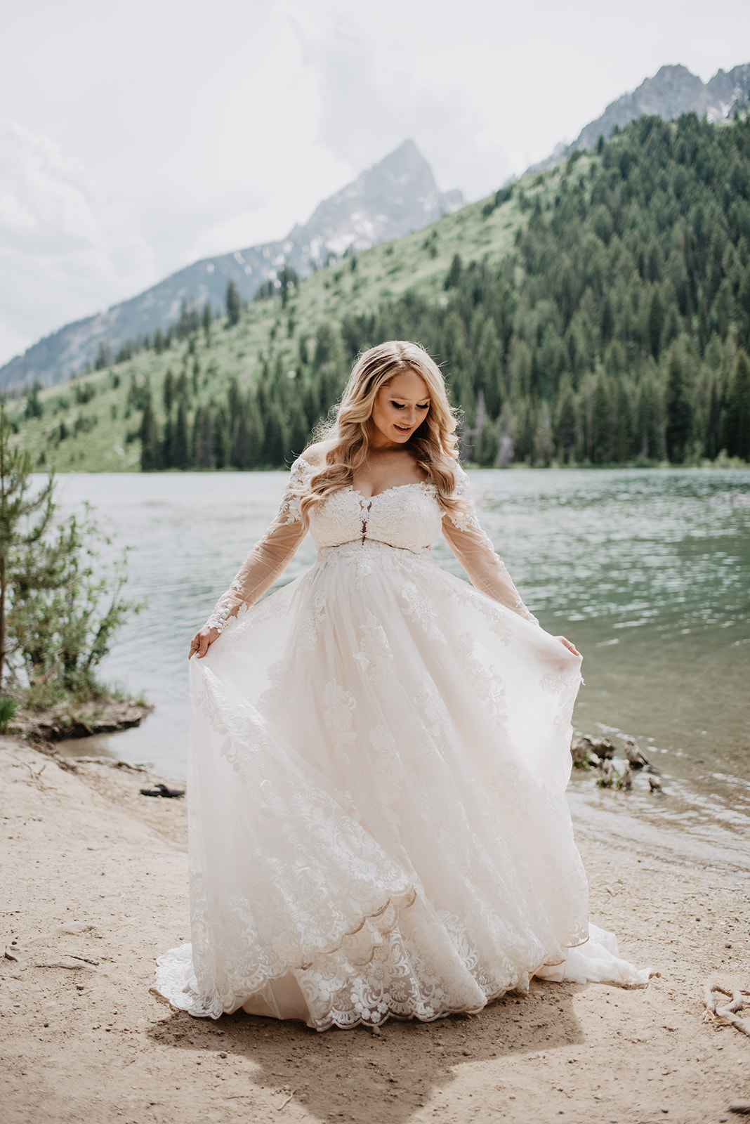 beautiful pregnant bride twirling in her full length flowy wedding gown in front of a lake in Jackson Hole for her wedding day at Diamond Cross Ranch