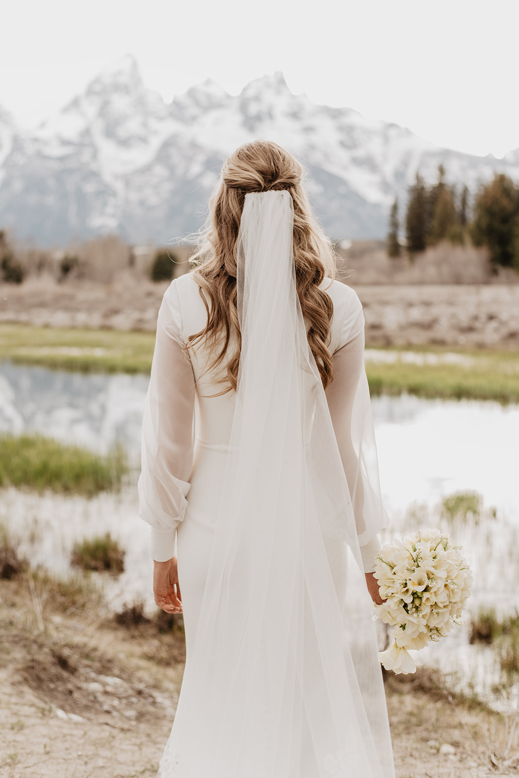 blonde bride facing away from the camera towards the Tetons mountain range on her Jackson Hole wedding day