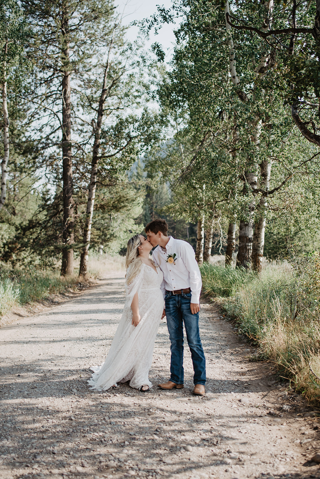 best venues for weddings in Jackson Hole with bride a groom walking on a dirt path in the woods of the Tetons and kissing