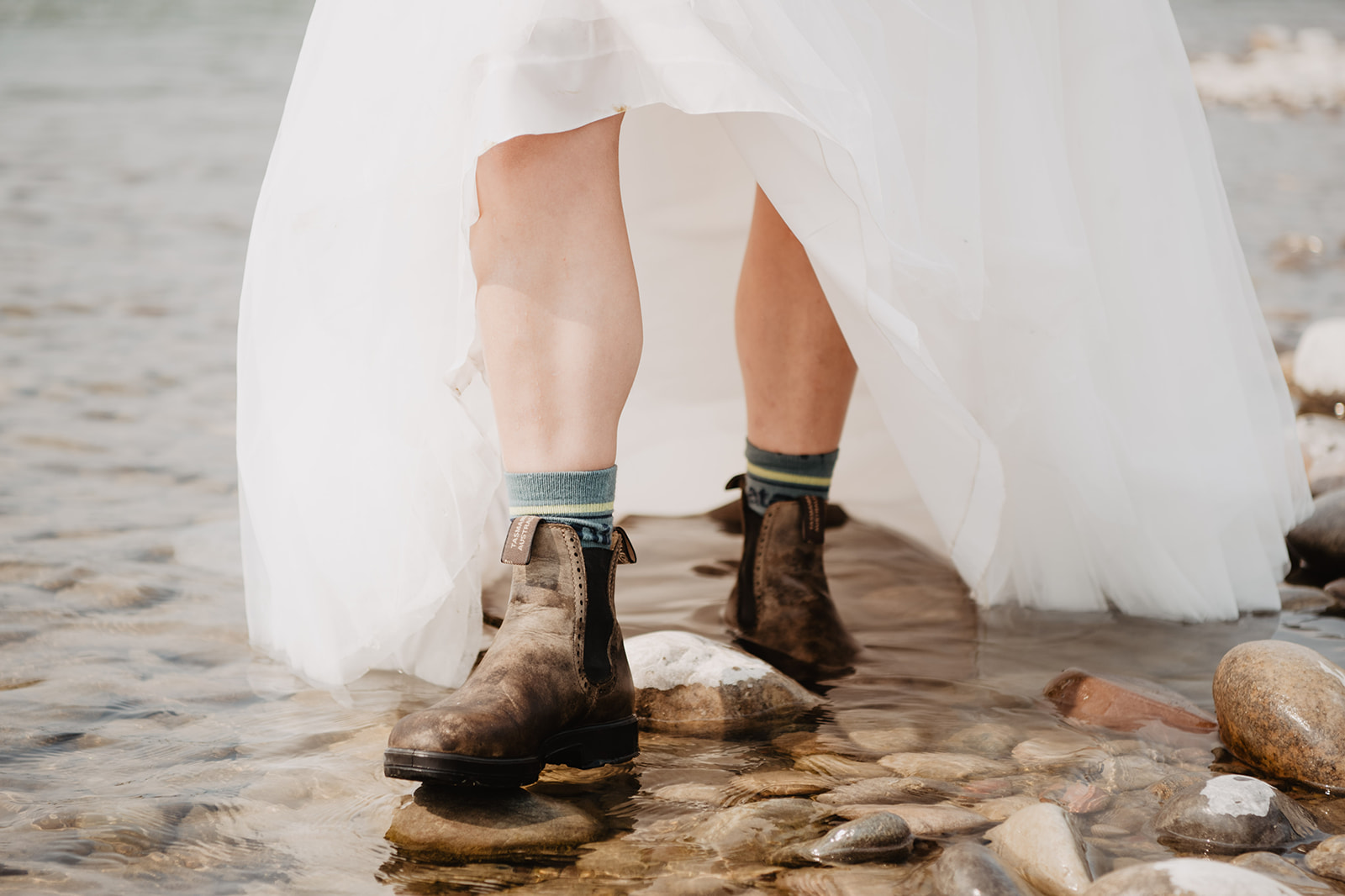 bride walking through a river bed in her hiking boots while she is wearing her wedding dress for her Jackson Hole elopement