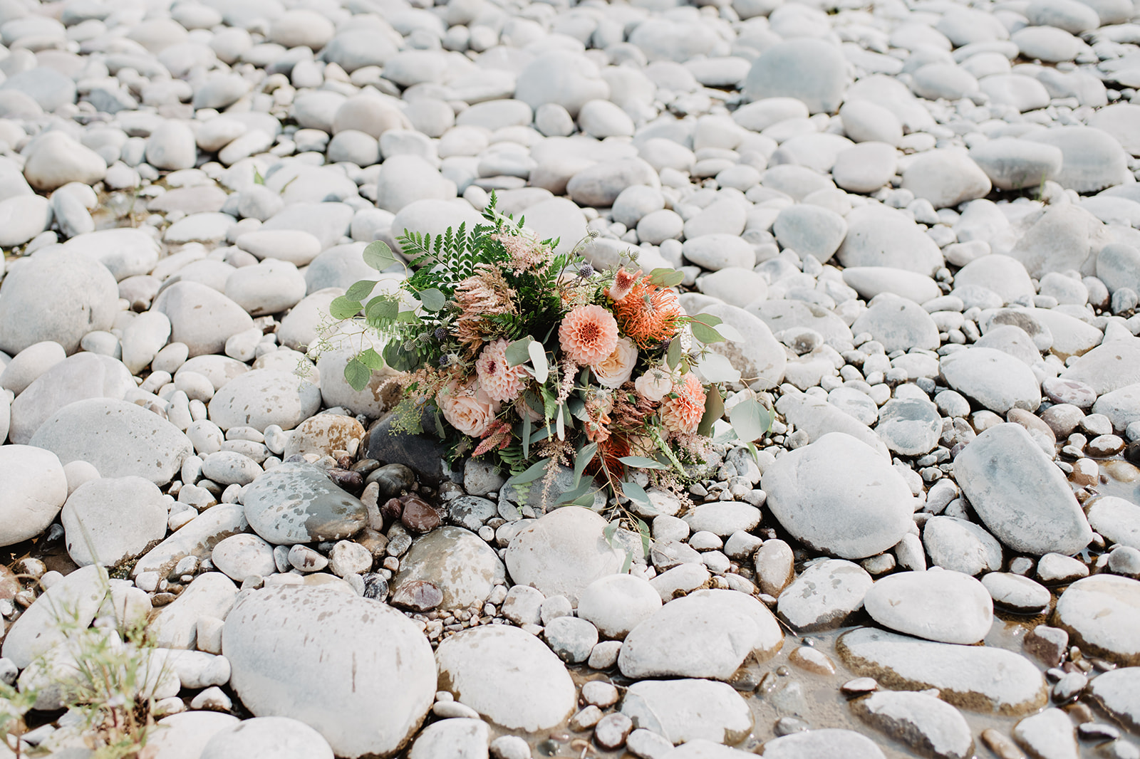 bridal florals bouquet with light pink flowers sitting on river rocks in Jackson Hole for an elopement