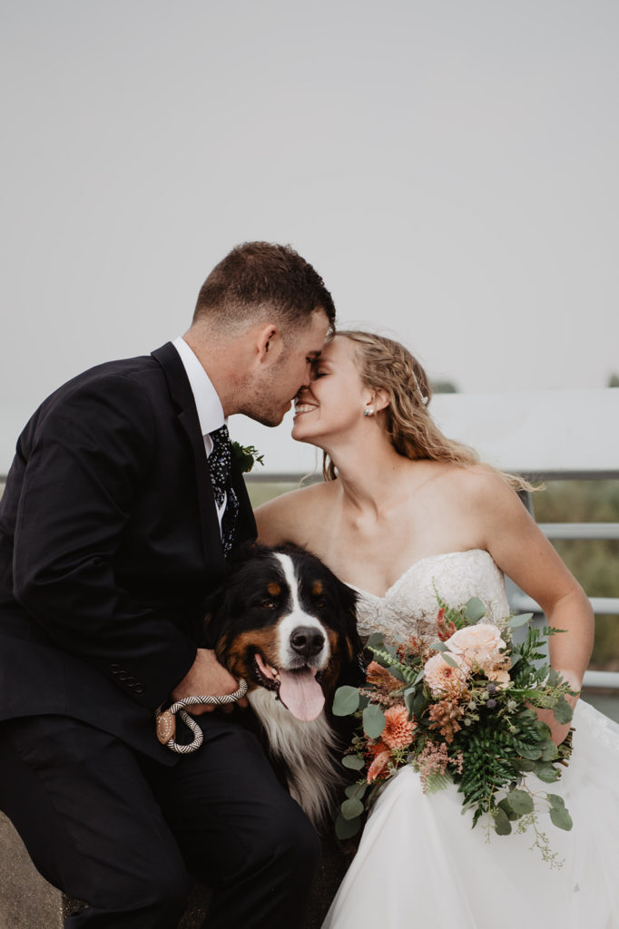 bride and groom leaning in for a kiss on a smoky wedding day in the Tetns with their dog between them, outdoor wedding with a dog