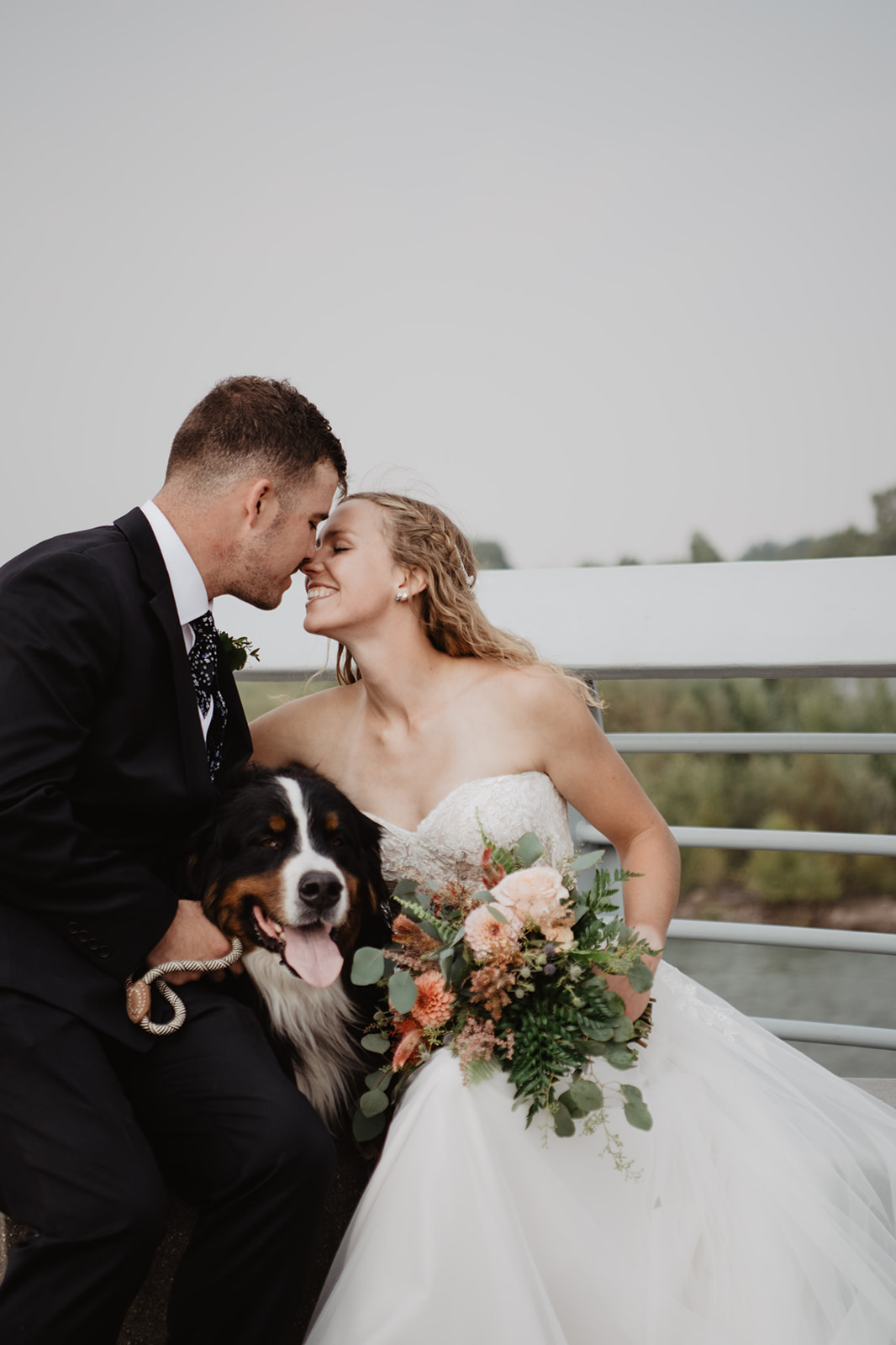 bride and groom embracing each other as they sit together on a bench on a bridge with their dog on their laps for their Jackson Hole wedding