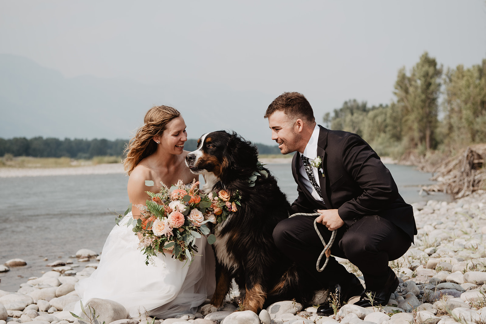 include your dog in your Grand Teton wedding at a location near a river with the bride and groom kneeling by their sheep dog