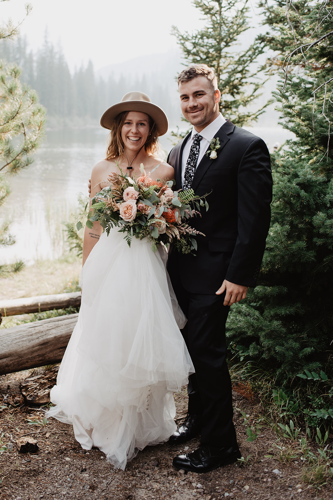 bride and groom hiking through the Tetons in their wedding day apparel with bride wearing a fun hiking hat