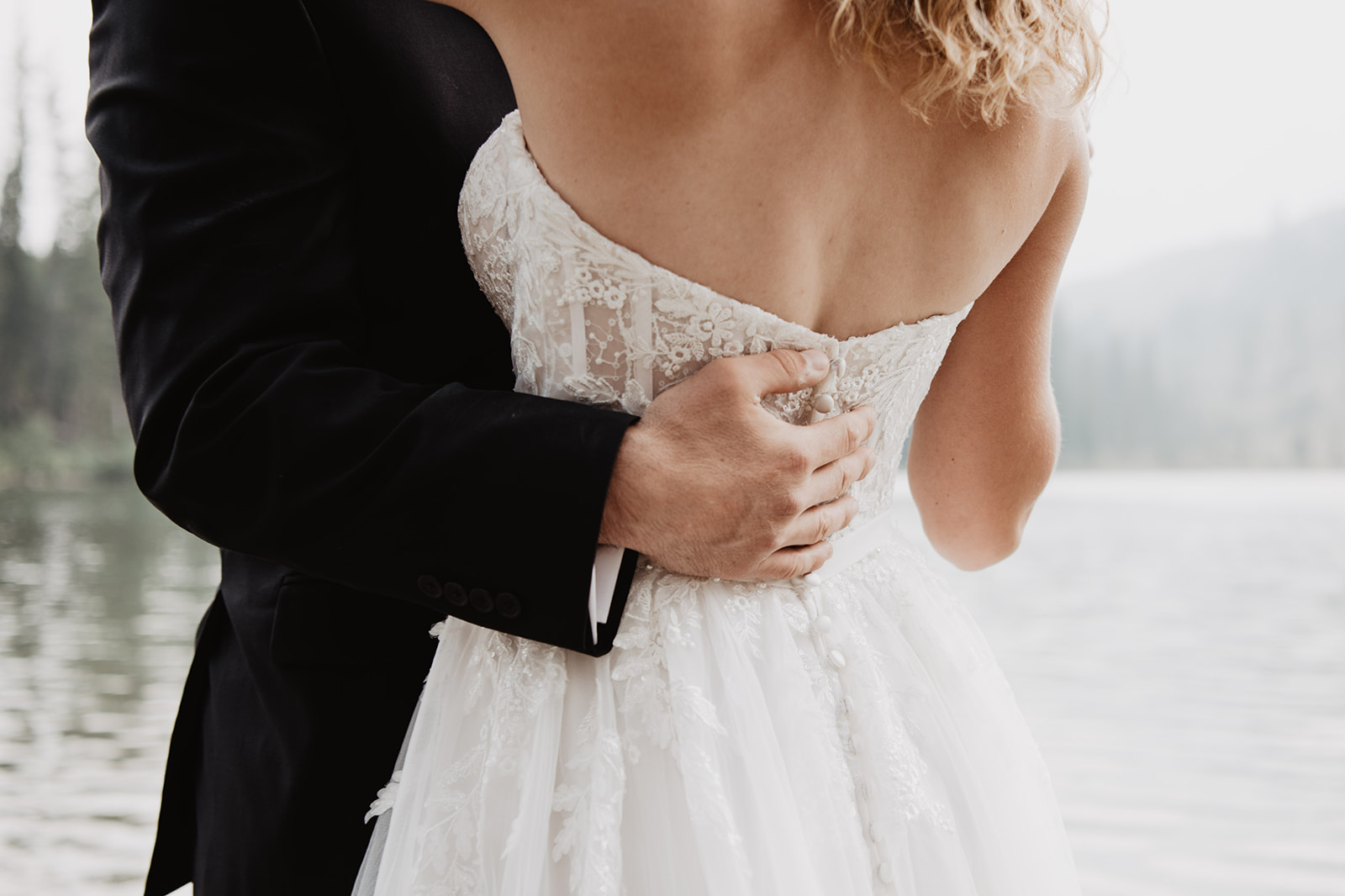 detail shot of the back of a brides corset bodice wedding dress with light lace as her groom holds her waist in Jackson Hole for an adventure wedding with best Jackson Hole wedding photographer