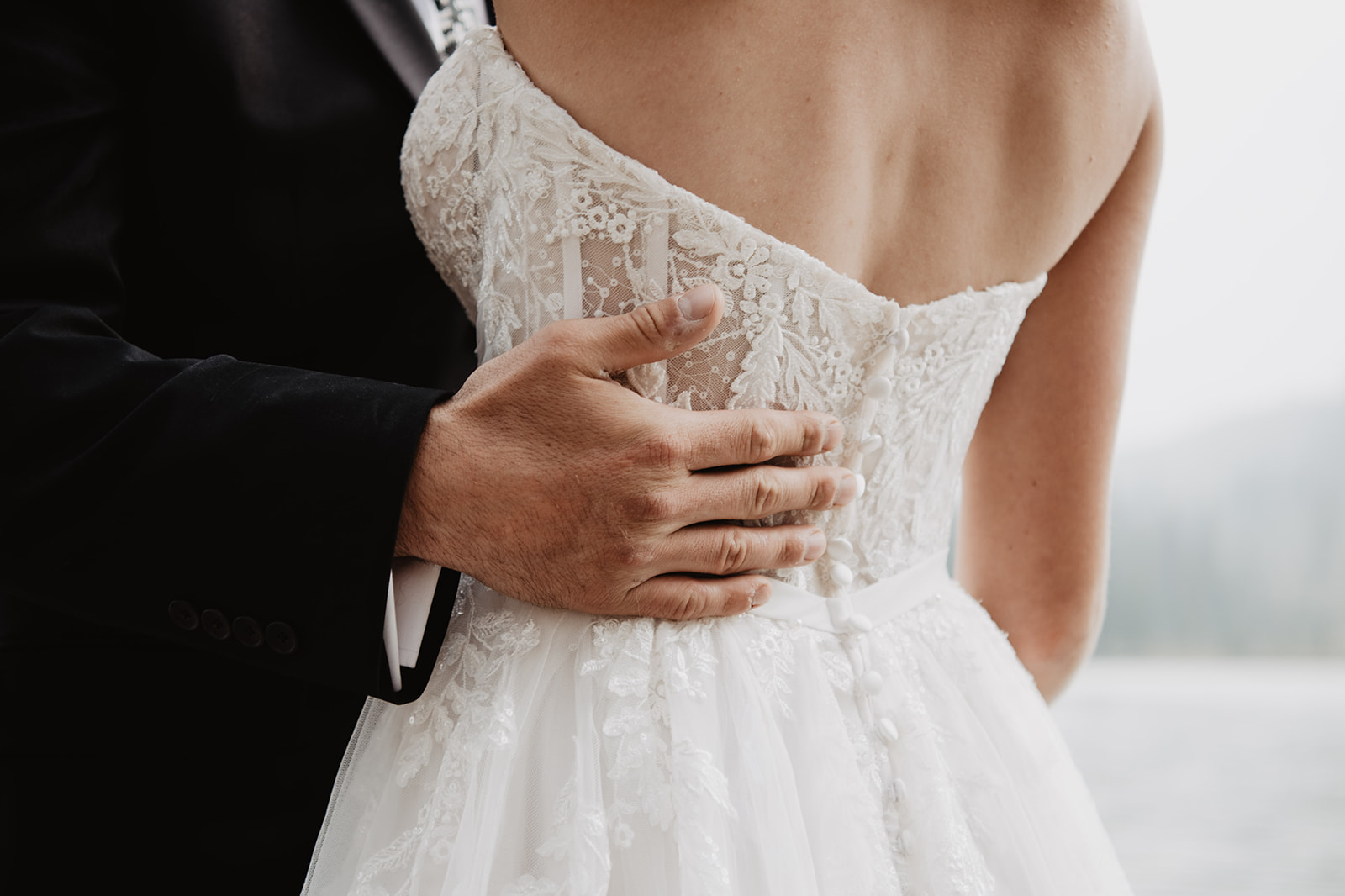 detail shot of the back of a brides lace dress while the groom holds her back as they are dancing