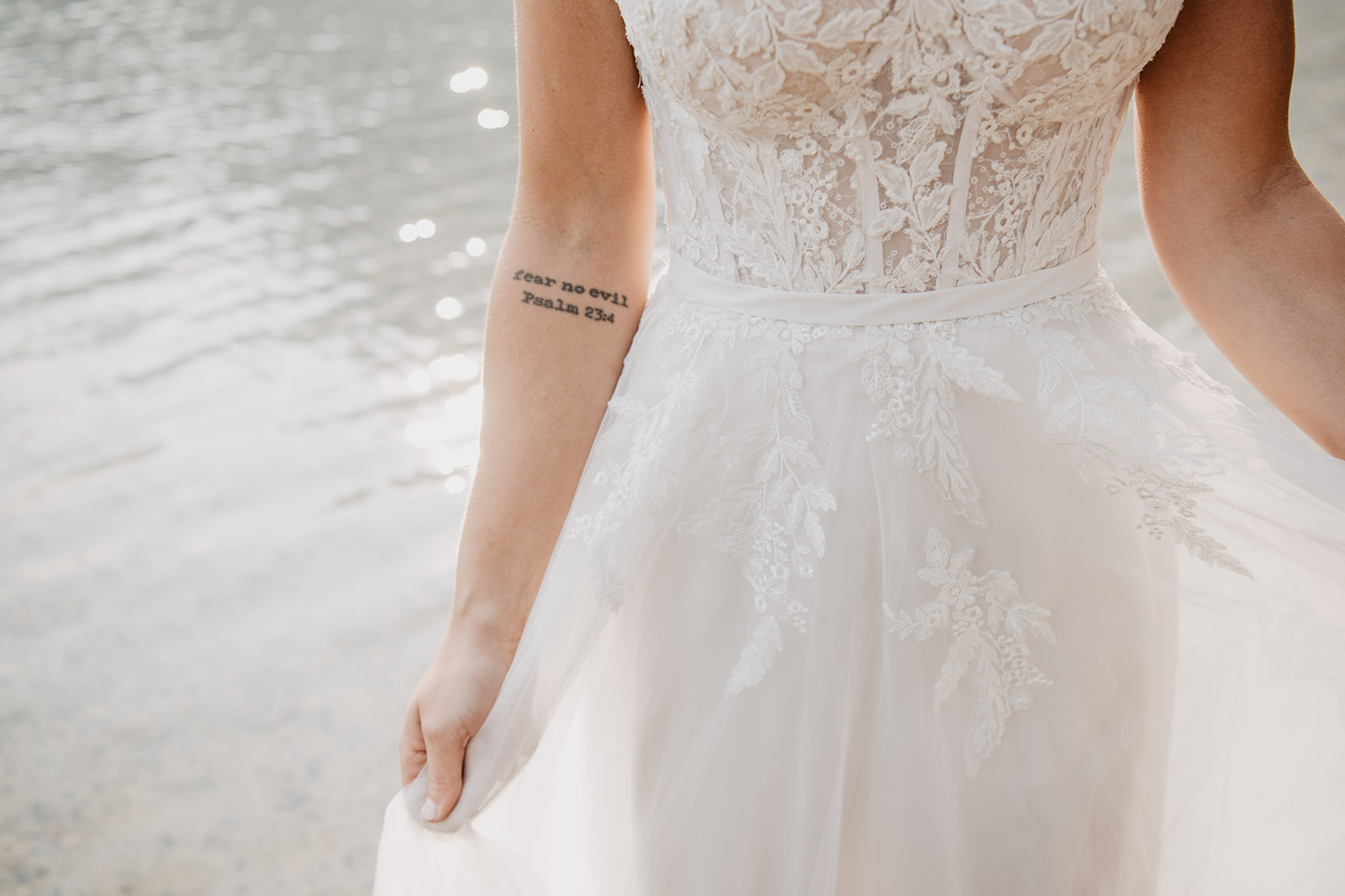 bridal detail shot of brides wedding dress as she is in the water at a lake in the Grand Tetons with her lace wedding dress that has a corset bodice
