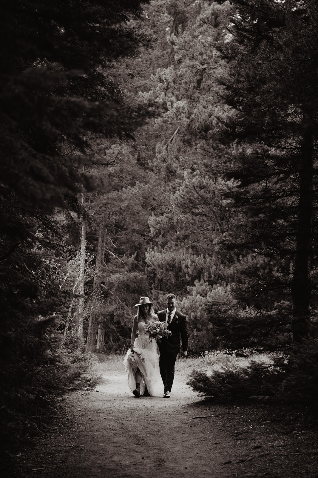 Jackson Hole wedding with bride and groom walking through the forest while holding hands on their adventure elopement, black and white wedding photo