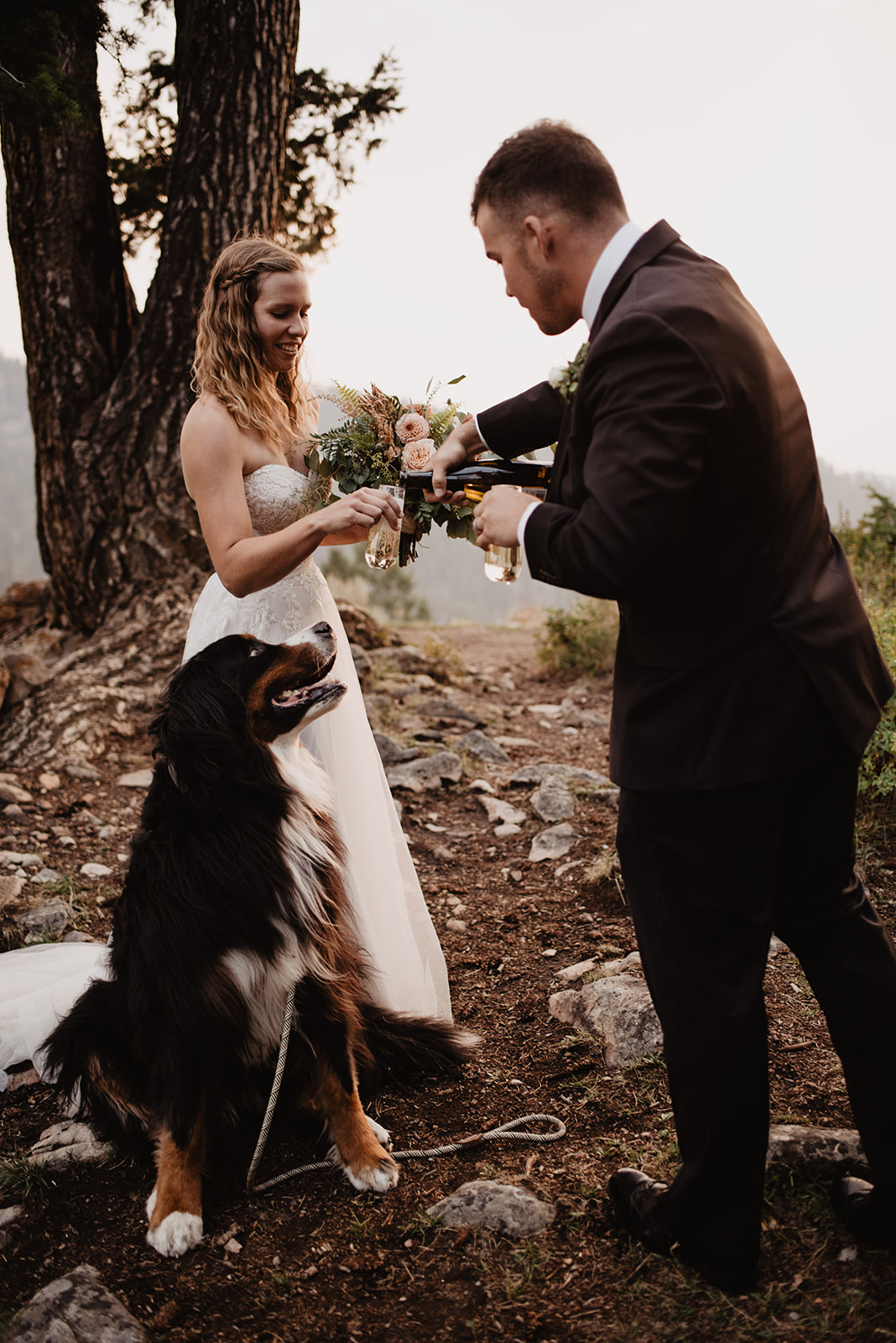 groom pouring champagne at the Wedding Tree in Jackson Hole with his bride and their dog as the sun sets over the Tetons