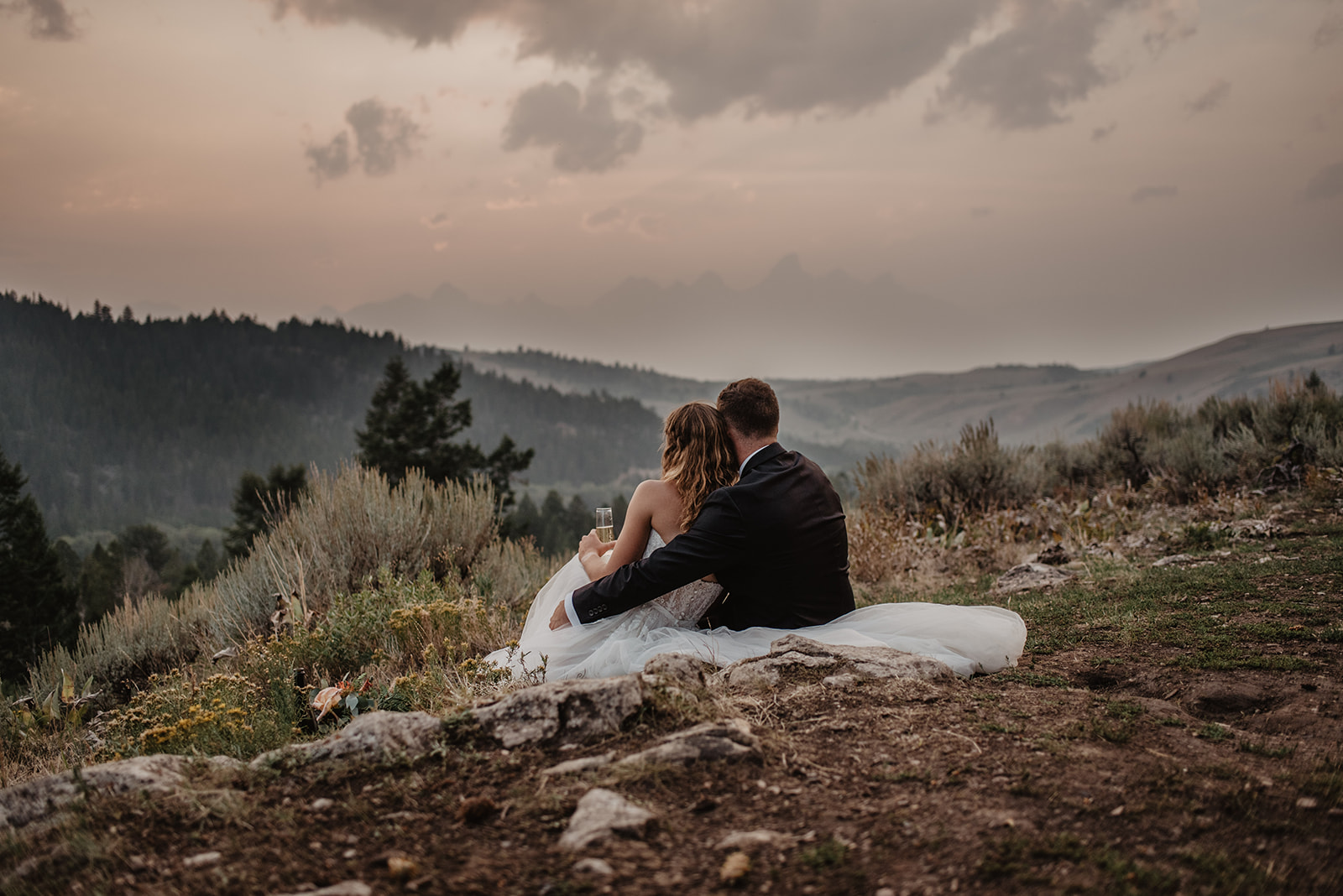 dark sunset photo with bride and groom sitting at the Wedding Tree in Jackson Hole looking out into the valley and at the Tetons in the distance at the end of their adventure elopement session