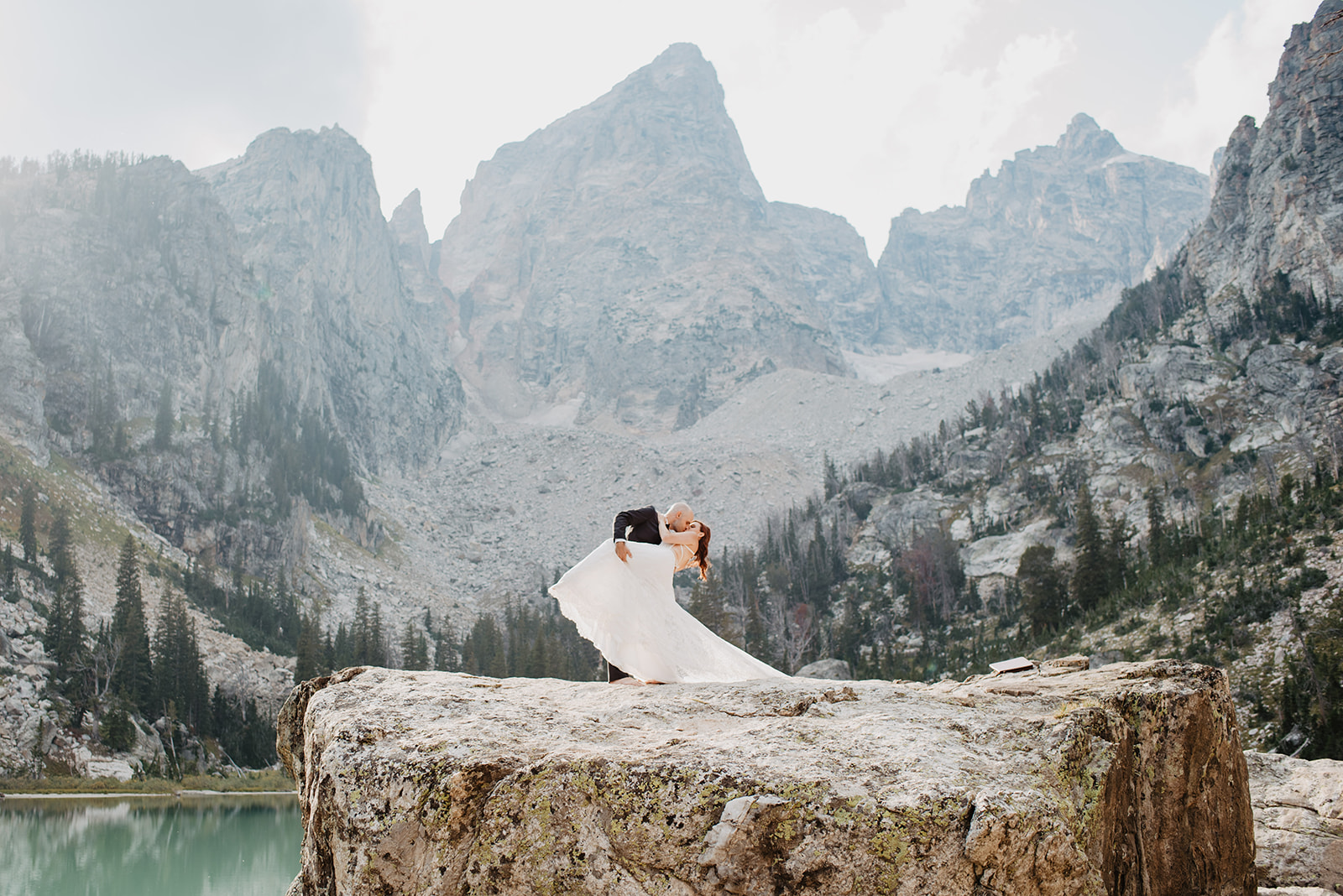 wedding dress ideas for 2022 with glacier lake fall elopement in the Grand Teton National Park with bride being dipped by her groom as her wedding dress flares out beneath her as they kiss with the majestic mountain range behind them in Wyoming