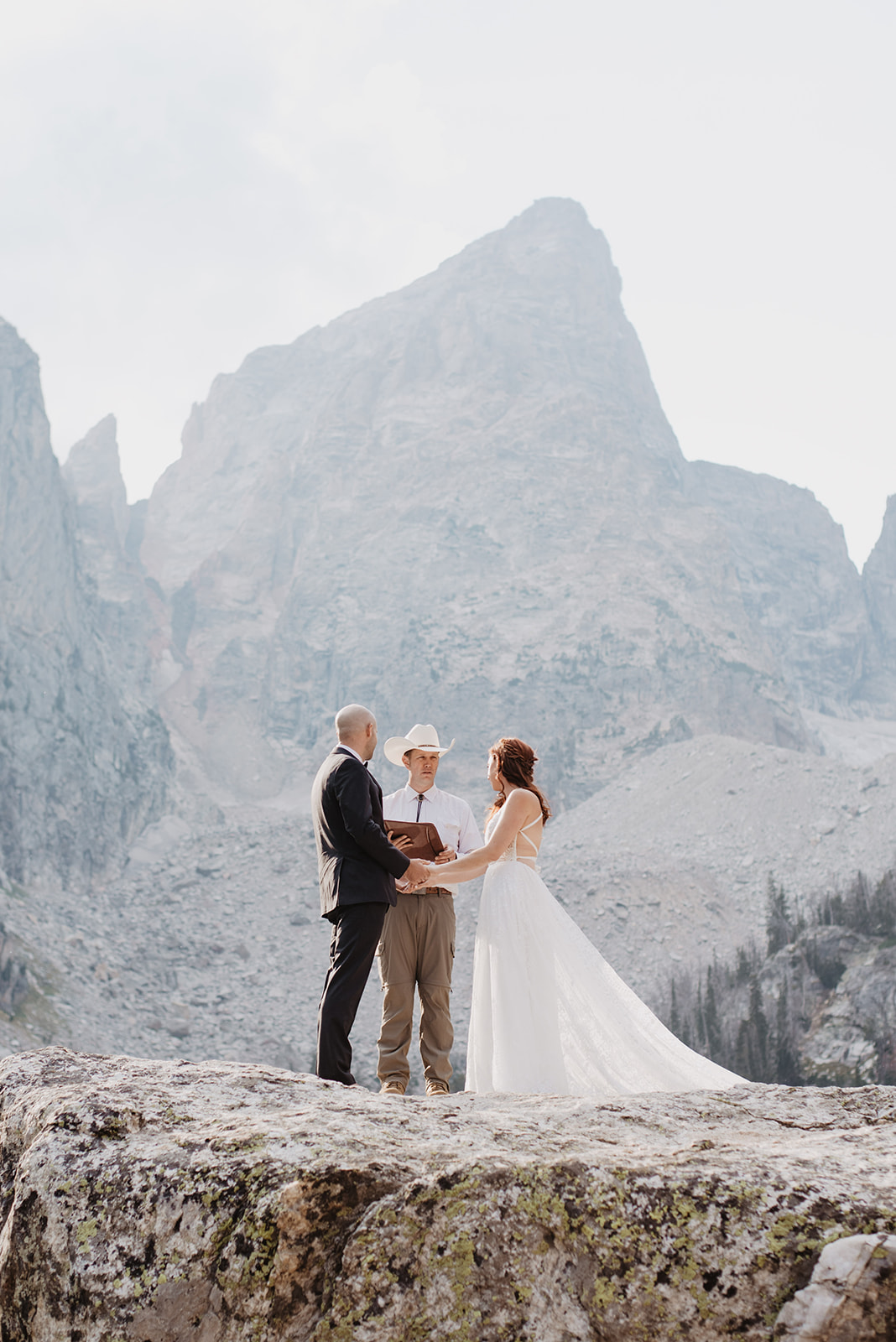 Delta Lake elopement in the Tetons with bride and groom standning on a boulder with their wedding officiant with the Grand Tetons mountains behind them for an adventure elopement