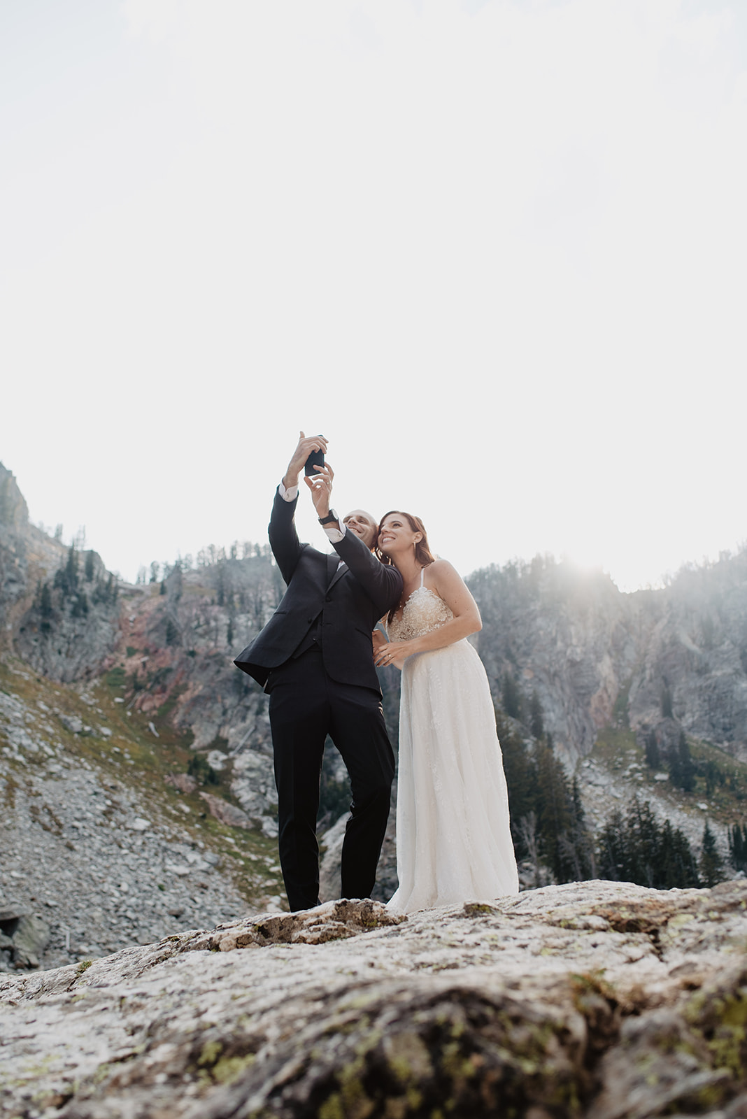 bride and groom in the Tetons at a glacier lake holding hteir cell phone to facetime with a friend who could not make it to their elopement