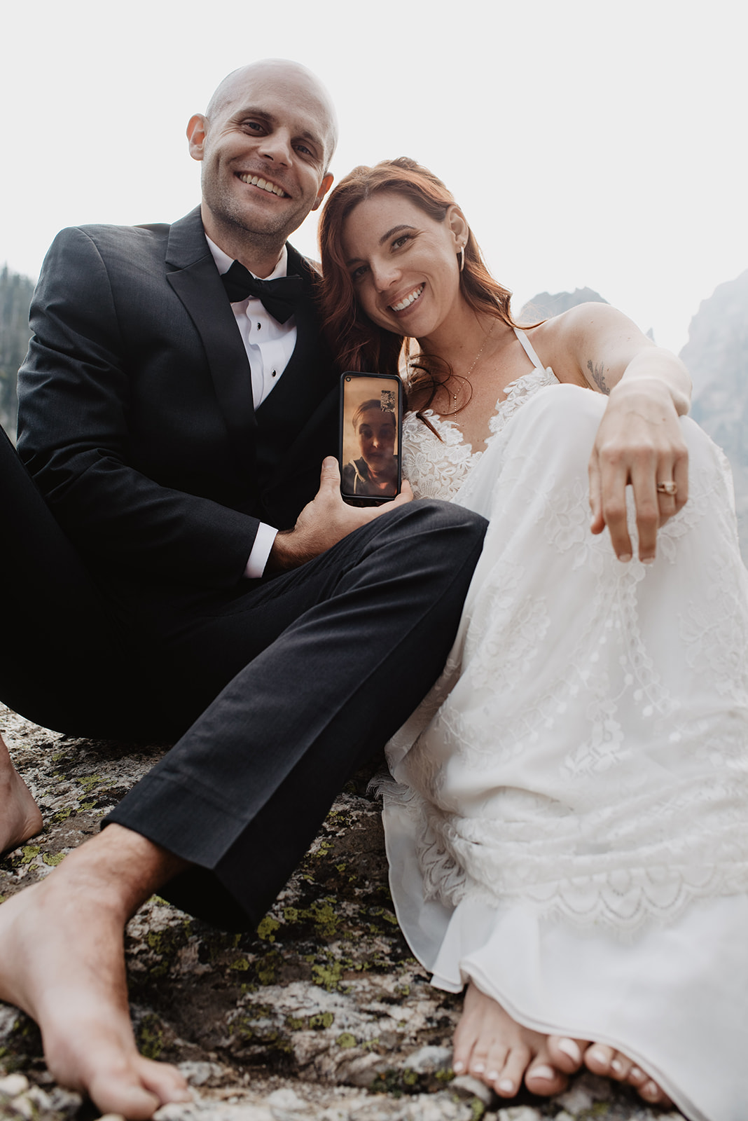 bride and groomin the Grand Tetons hold their iphone while facetiming a friend to take a group photo to show how to include loved ones in your elopement when they cannot make it