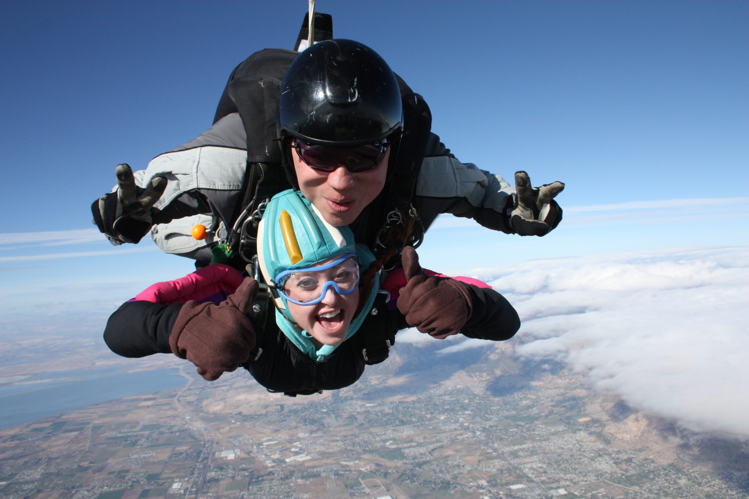 adventure elopement photographer goes skydiving and posing with a thumbs up as she is mid air smiling