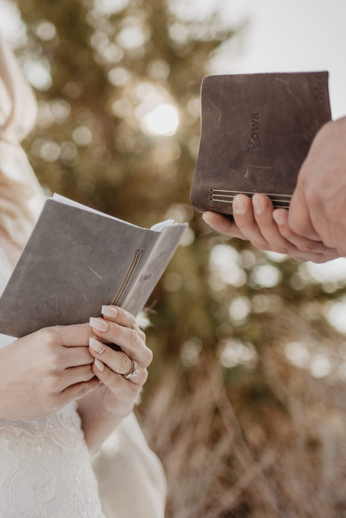 bride and groom hold leather bound, grey and brown vow books in Jackson Hole at their winter elopement