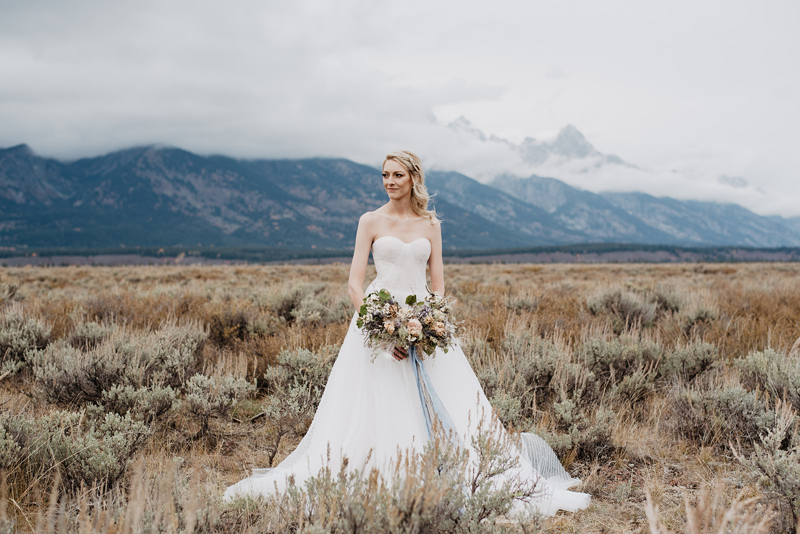 bride in a field right before it is about to rain in Jackson Hole with the mountains behind her