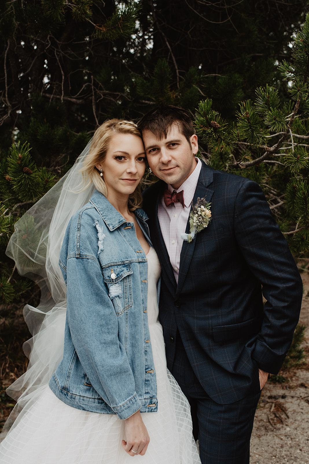 Bentwood Inn weddings bride in a cute demin jacket with her new last name on the back while standing next to her groom who is in a blue suit as they both smolder at the camera while standing in front of evergreens in Jackson Hole, taken by Jackson Hole wedding photographers