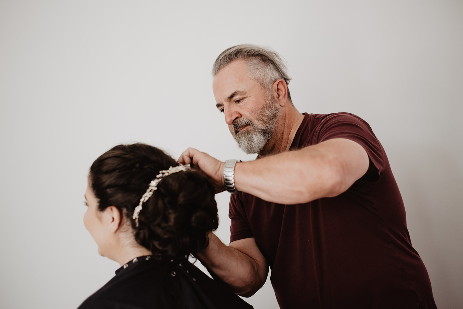 bride getting her hair done by her father in law on her wedding day with an up-do and a crystal band around her bun
