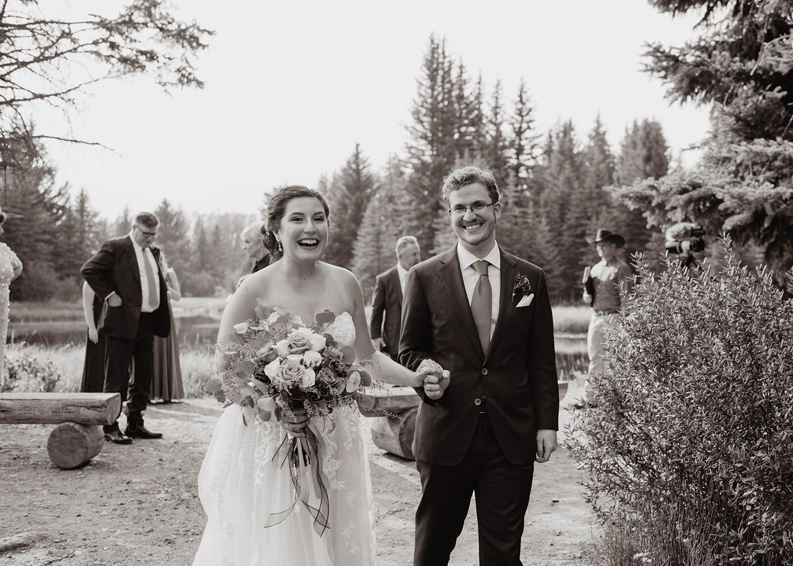 black and white picture of bride and groom walking away from their natural wedding alter with bride laughing and happy and groom grinning. Jackson Hole wedding photography