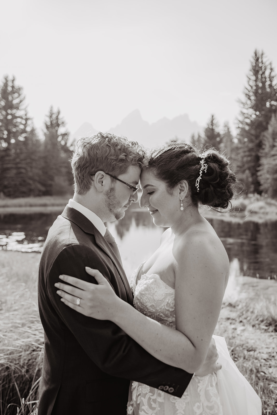 black and white image of bride and groom with their foreheads together with the Tetons behind them