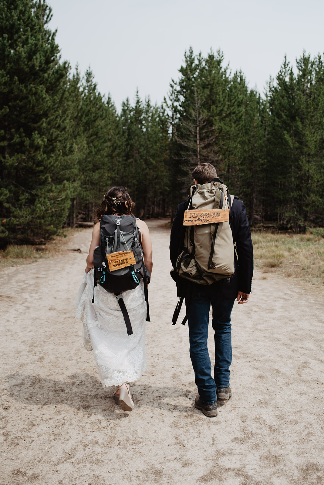 bride and groom hiking together on a trail with their backpacks on with just married signs on their packs for the Grand Tetons wedding day