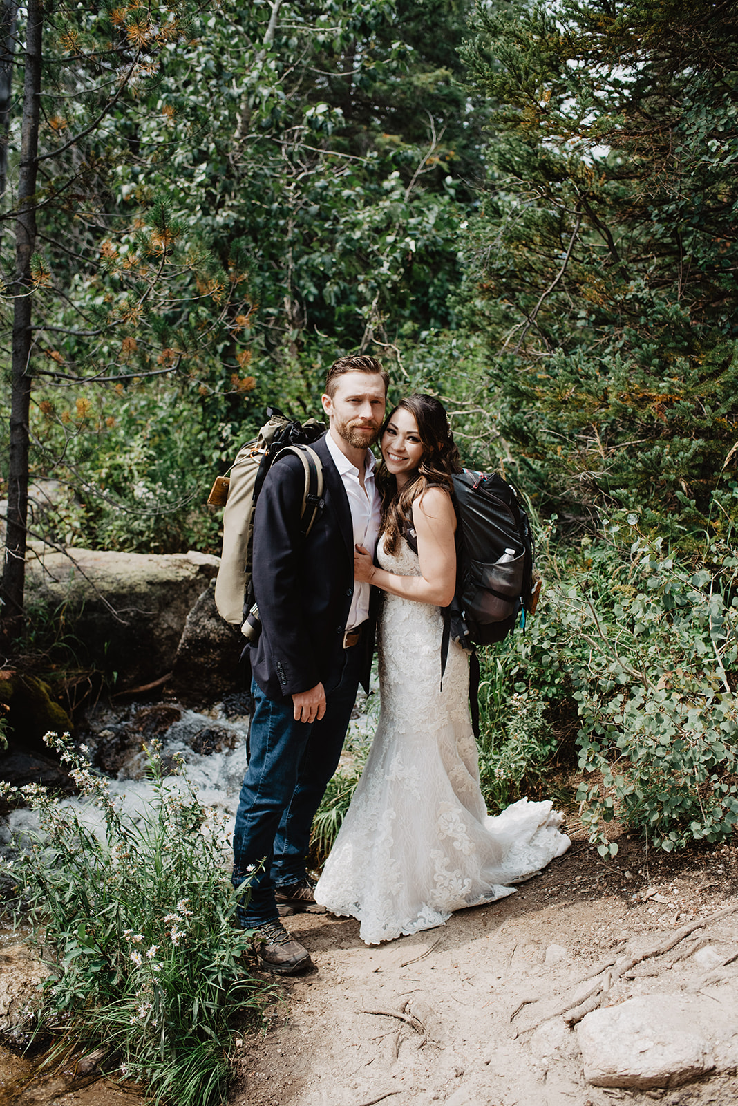 bride and groom posing next to a small creek in the Tetons as they hike on a trail with their packs on during their adventure wedding in Grand Teton National Park Wedding